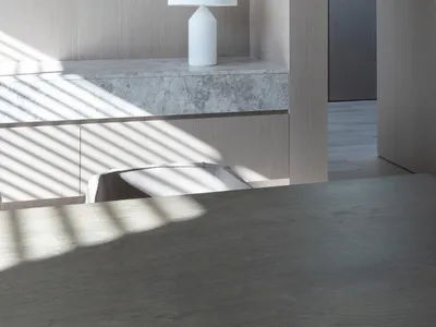 A minimalist living room with concrete walls, a gray textured floor, and a white table lamp.