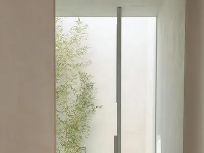 A minimalist bedroom with a bed draped with a neutral-toned textile, surrounded by natural light and greenery.