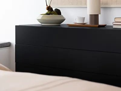 Minimalist bedroom featuring a black sideboard with a plant, a cup, and a lamp.