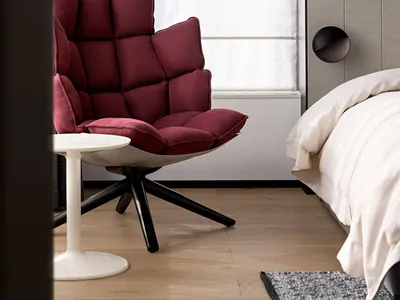 A minimalist bedroom featuring a luxurious red upholstered chair, a comfortable bed with a neutral-toned quilt, and a modern,