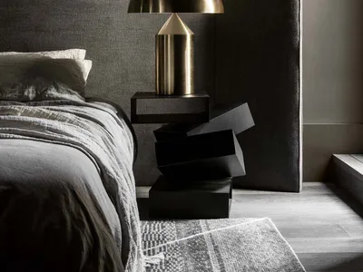 A minimalist bedroom with a metal side table, grey bedding, and a grey headboard.