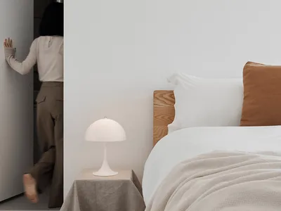 A minimalist bedroom with a white wall, wooden bed frame, and beige bedding.