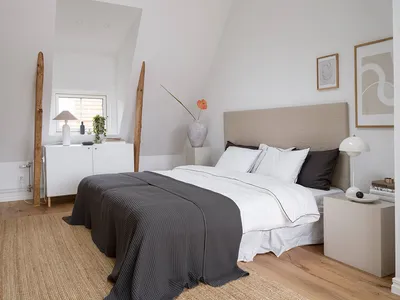 Modern minimalist bedroom with wooden flooring, fabric bedding, and ceramic vase.