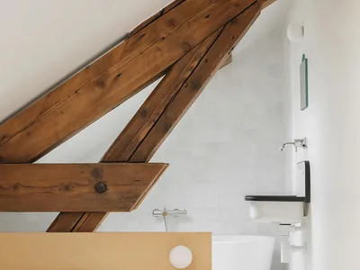 A minimalist bedroom with white walls, a wooden bed frame with a white mattress and pillows, and wooden beams on the ceiling.