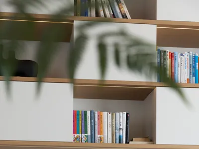 A minimalist home office with a wooden desk, white surfaces, and various books organized on shelves.