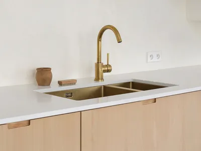 A minimalist residential kitchen with wooden cabinetry and a gold-finished sink.