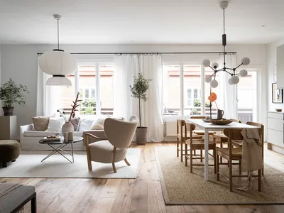 A modern Scandinavian living room with a minimalist design, featuring a white sofa, cushioned armchair, and wooden dining tab