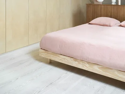 Modern minimalist bedroom featuring a wood platform bed with pink bedding, situated in a slanted ceiling room with exposed wo