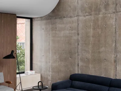 A minimalist living room featuring a concrete wall and floor, with a navy blue sofa and a dark wood coffee table.