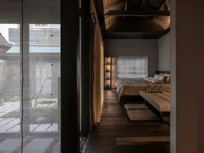 A minimalist bedroom with a wooden floor, a bed with simple bedding, and a low bench for seating.