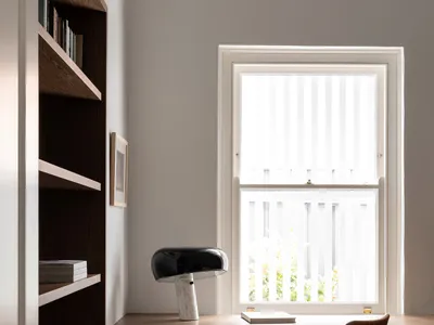 A modern home office with a desk, chair, and lamp next to a bookshelf.