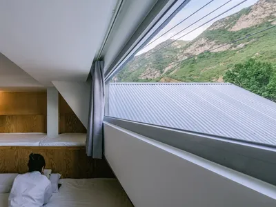 Minimalist bedroom with wooden walls and a view of the mountains outside a large window.