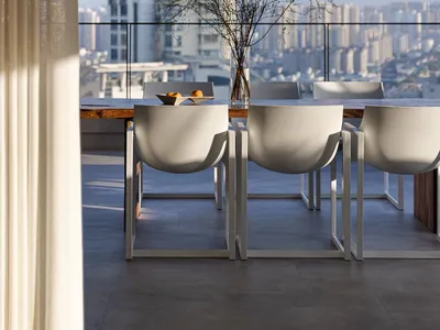 A minimalist living room featuring a concrete floor, white chairs, and a vase with branches, with a cityscape view in the bac