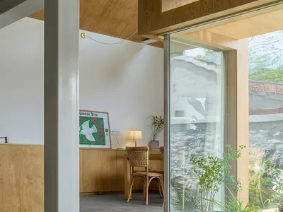A modern home office with wooden walls, concrete floor, and a desk with a lamp and a chair.