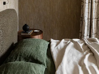A minimalist bedroom featuring a green bed and wood side table.