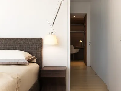 A modern minimalist bedroom with a wooden floor and a bed covered in fabric.