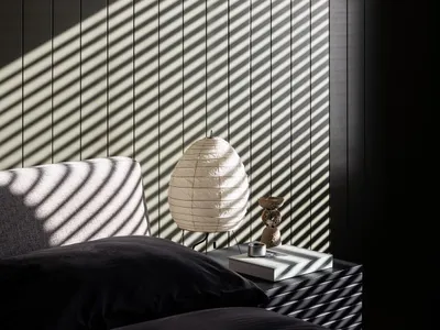 A minimalist bedroom with a black iron bed frame and wooden flooring, featuring a lamp and books on a nightstand.