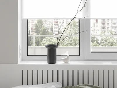 A minimalist bedroom with a white blanket and gray blanket on a bed, featuring a vase with a branch and a bird figurine on a