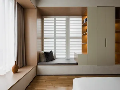 A minimalist bedroom with a wooden seating area by the window, featuring a cushion and a vase on the ledge, and a built-in bo