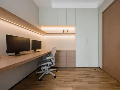 A modern home office featuring a desk with two monitors, a chair, and black storage units.
