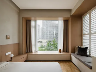 Minimalist bedroom with large windows, wooden walls, and a white bed.