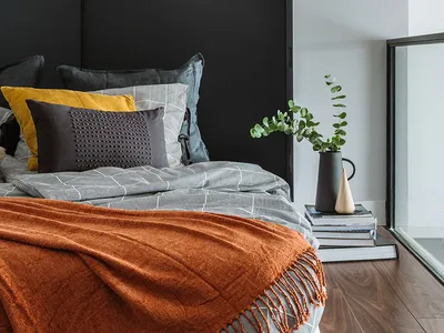 Minimalist bedroom featuring a bed with a dark headboard and mixed texture bedding, along with a small plant on a stack of bo