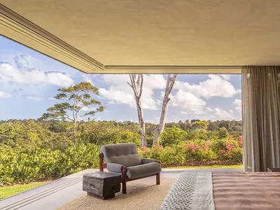 A minimalist bedroom featuring neutral colors and a view of lush greenery outside.