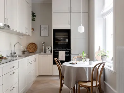 A minimalist white kitchen with a round table and chairs by the window.