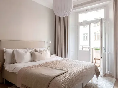 A minimalist bedroom featuring a bed with fabric bedding and wooden furniture, natural light streaming through the window.