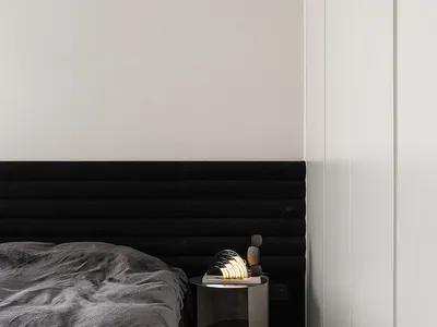 A modern minimalist bedroom featuring a black upholstered bed and a metallic bedside table with a modern lamp.