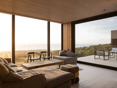 A luxurious coastal living room featuring wooden furniture, large windows overlooking the ocean, and a comfortable sectional