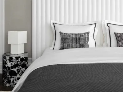 A minimalist bedroom featuring a white fabric headboard and a marble side table.