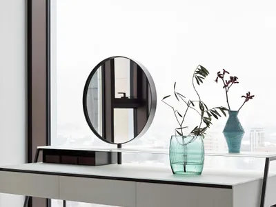 Modern, minimalist office workspace featuring a sleek white desk and round mirror in front of a large window with a snowy cit