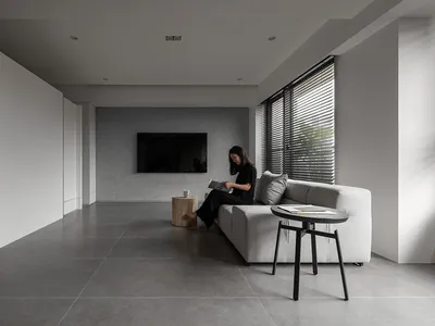現代極簡客廳，鋪設混凝土地板，搭配白色沙發，一位女士坐在百葉窗旁的窗邊閱讀