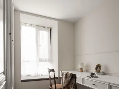 A minimalist home office with a wooden desk, white walls, and sheer curtains by the window.