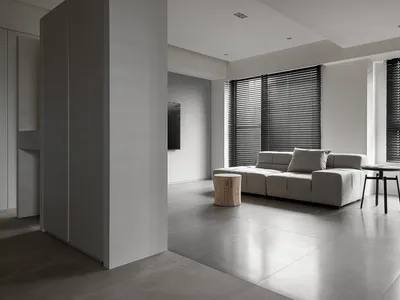 Modern minimalist living room with concrete flooring, a gray sofa, and black window blinds.