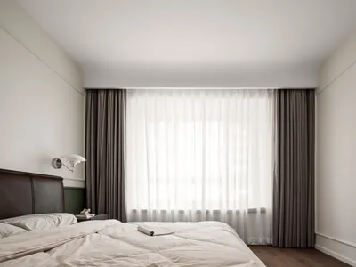 A minimalist bedroom featuring fabric curtains and wooden floors.