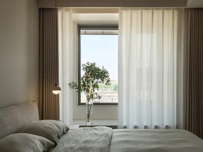 A minimalist bedroom with a bed, pillows, and curtains by the window.