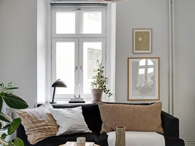 A minimalist living room with a black sofa, wooden side tables, and a modern pendant light.