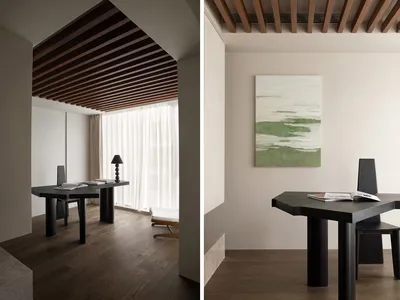 A minimalist home office space featuring black furniture, wooden ceiling beams, and a window with white curtains.