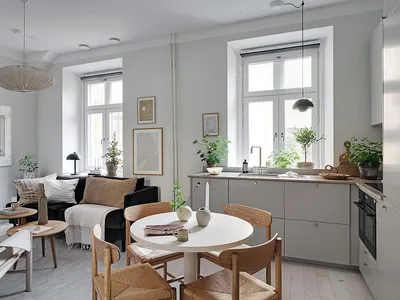 A minimalist residential space featuring a white dining table surrounded by wooden chairs, a grey sofa with white cushions, a