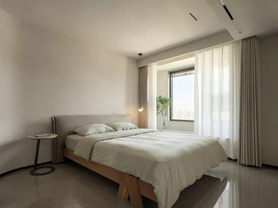 Modern minimalist bedroom with light neutral tones, featuring a comfortable bed with a simple wooden frame and upholstered he
