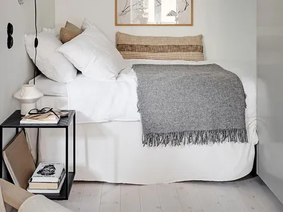 Minimalist bedroom featuring neutral-toned walls, bed with white bedding and gray throw blanket, and framed artwork.