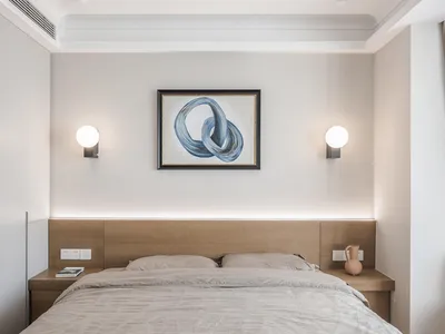 A minimalist bedroom with a wooden headboard and fabric bedding, featuring a framed abstract painting with blue shapes and a