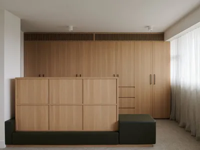 極簡公寓客廳室內視圖，展示木製櫃體牆面與綠色腳凳。