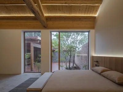簡約臥室擁有木樑天花板與大型窗戶，窗外可眺望花園。