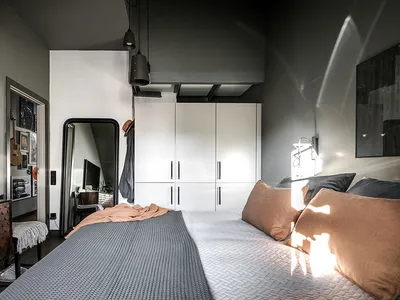 A minimalist bedroom with mixed materials, featuring a bed with grey and brown bedding, and a white wardrobe.