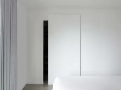 A minimalist bedroom with a white wall, bed, and sliding door.