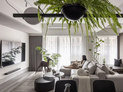 Modern, minimalist living room with concrete elements, plants, and a woman relaxing on a sofa.