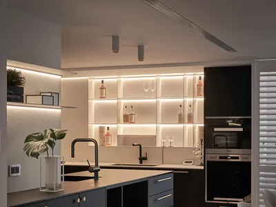 A modern minimalist kitchen with black wood cabinetry and black metal accents, featuring built-in lighting and a sleek, open